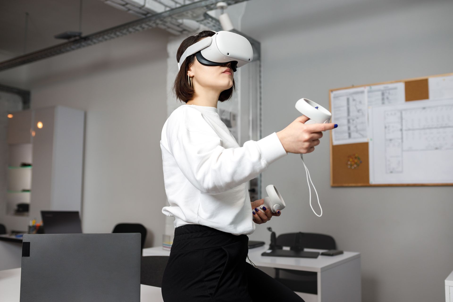 Person using a virtual reality headset and controllers in an office setting.