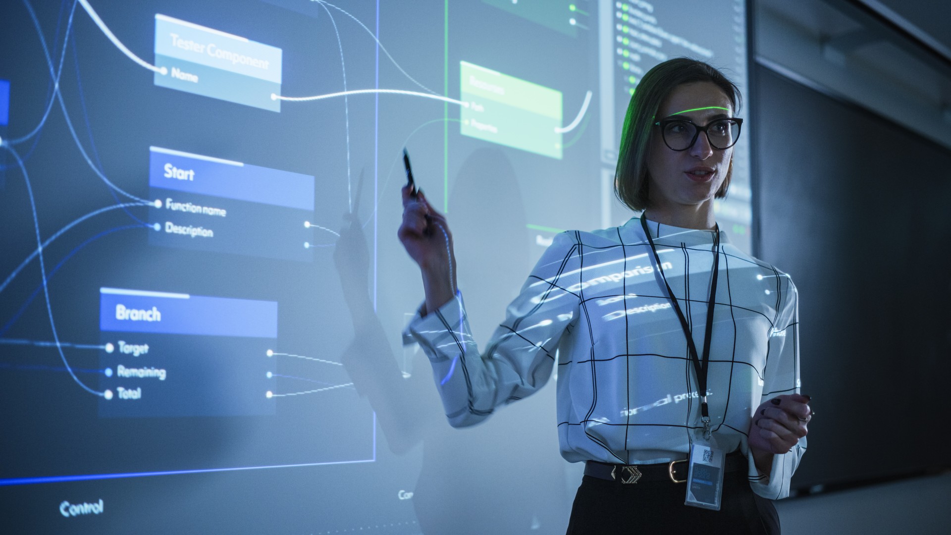 Portrait of a Young Female Professor Explaining Big Data and Artificial Intelligence Research Project in a Dark Room with a Screen Showing a Neural Network Model. Computer Science Education in College