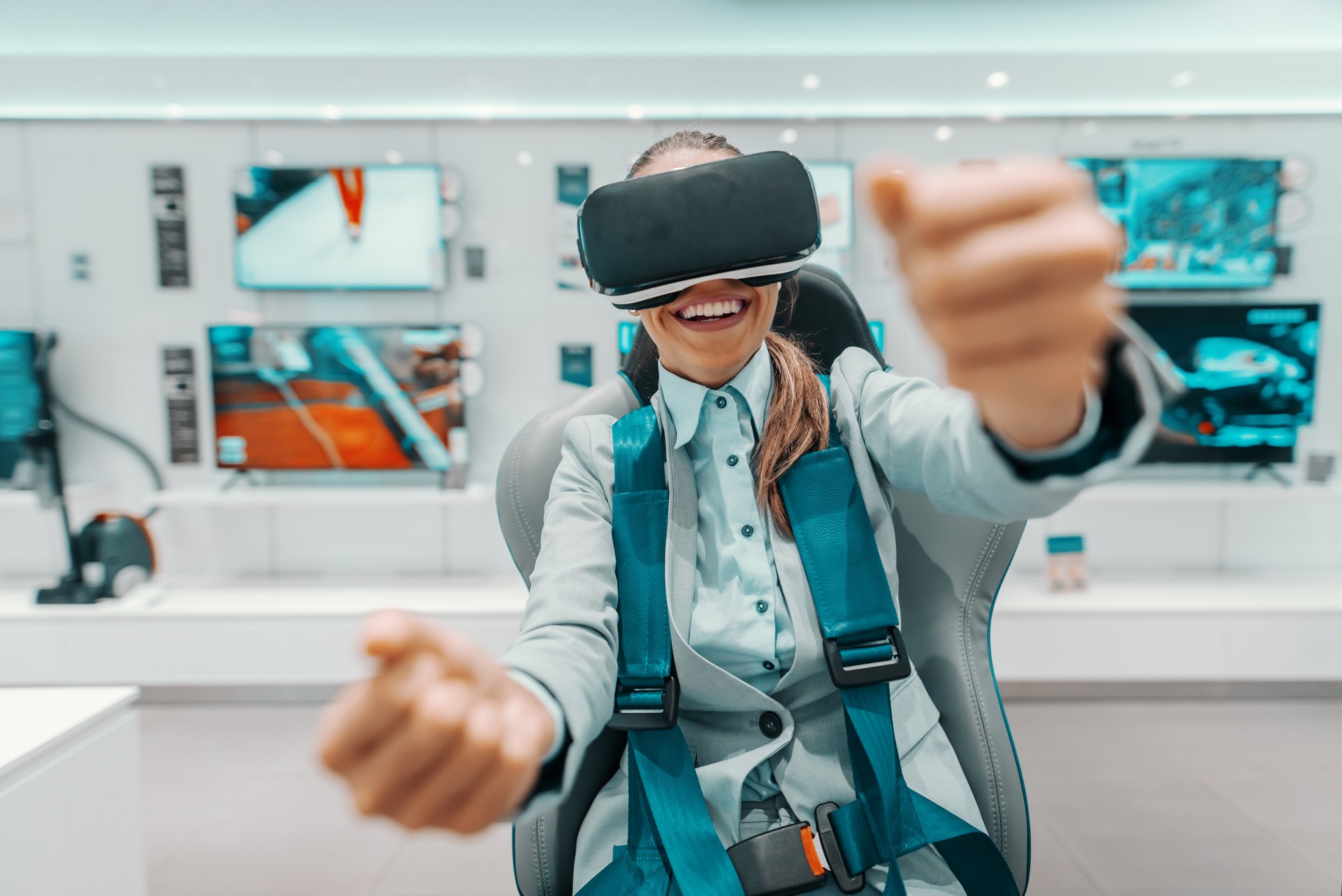 Smiling Caucasian woman in formal wear trying out virtual reality technology while sitting in the chair in tech store.